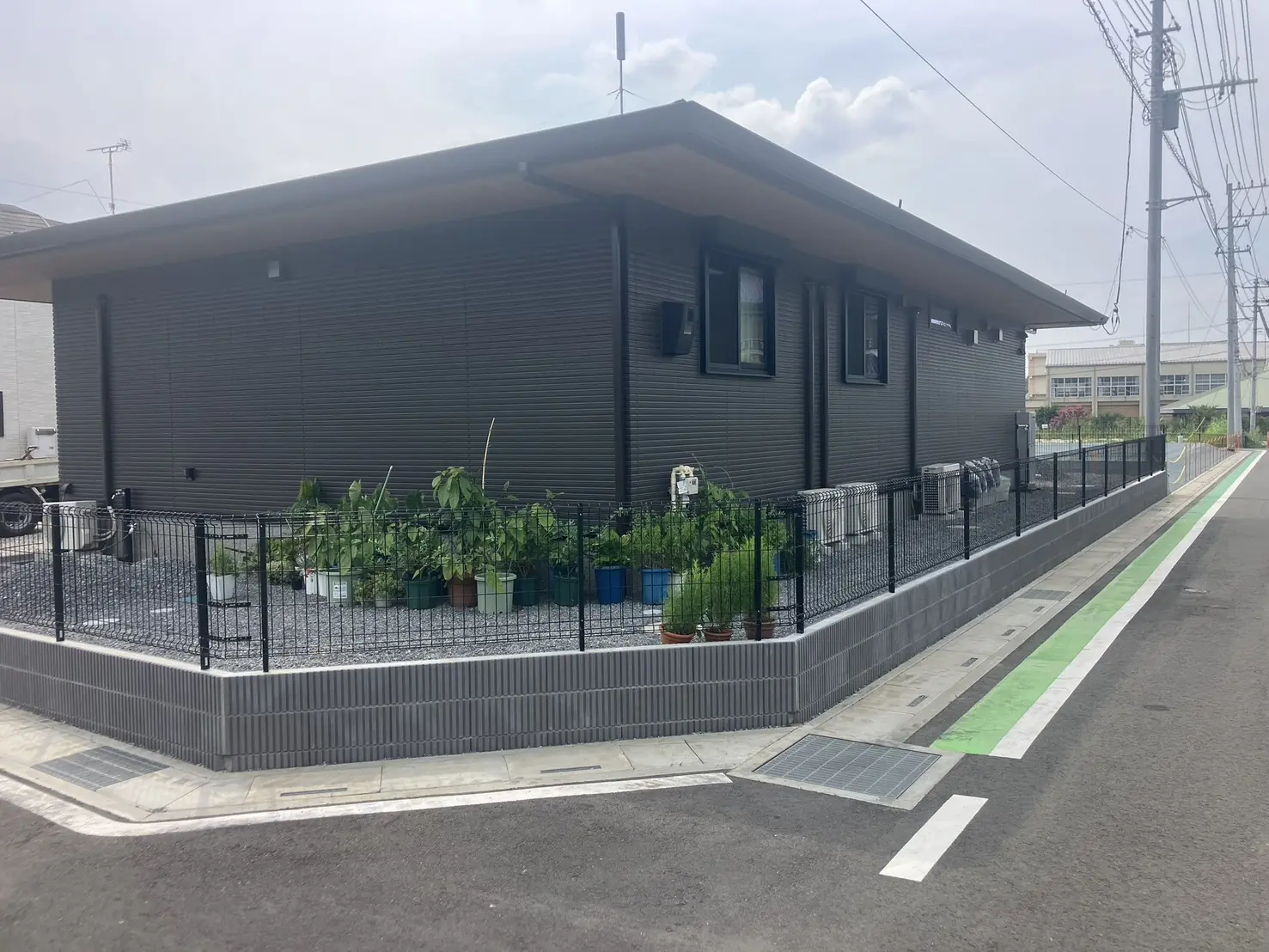 道路の角に沿って化粧ブロックとメッシュフェンスを設置した平屋の外構